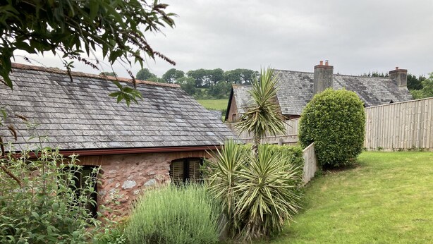 A rustic stone house with a sloped roof, surrounded by a well-maintained lawn and various shrubs. - Barn Conversion, 5 miles from the coast with own parking and garden (Collaton St Mary)