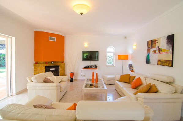 Uma sala de estar com lareira, sofás brancos, uma mesa de centro e uma televisão.