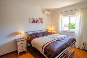 Um quarto com cama, mesas de cabeceira, janela e ar condicionado.