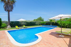 Piscina retangular com borda curva, cercada por um pátio de tijolos.