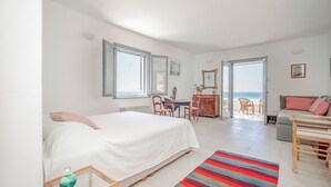Une chambre spacieuse avec un grand lit, un bureau et une vue sur la plage, accessible par une porte ouverte.