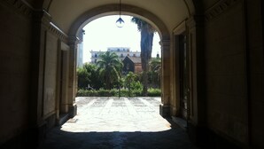 An arched corridor with a view of a building and palm trees in the distance.
