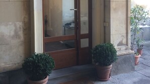 A building entrance with a double wooden door, a welcome mat, and two potted plants on either side.