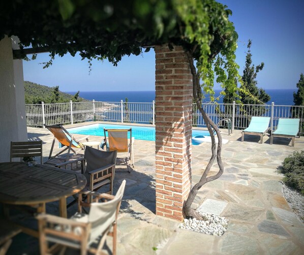 A poolside area with lounge chairs, a table, and a view of the sea.