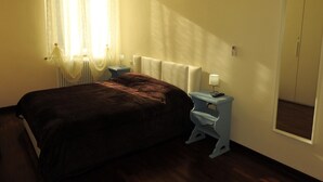 A bedroom with a bed, bedside tables, a lamp, a radiator, and a window with curtains. - Completely renovated apartment in the center (Ravenna)