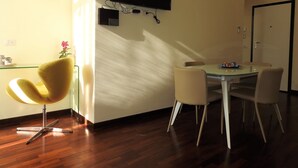 A modern dining area with a glass table, white chairs, and a yellow chair. A flat-screen TV is mounted on the wall above the table. - Completely renovated apartment in the center (Ravenna)