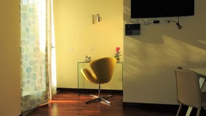 A room with a wooden floor, a yellow wall, a TV mounted on the wall, a chair, and a desk. - Completely renovated apartment in the center (Ravenna)