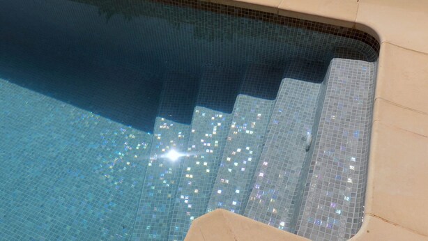 Una piscina con borde de azulejos y superficie de agua azul cristalina que refleja la luz.