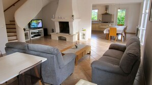 Un salón espacioso con chimenea, sofás grises, un televisor y un comedor con mesa y sillas.