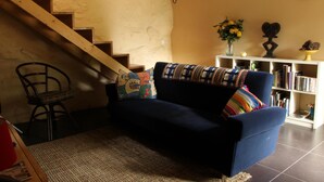 Een woonkamer met een blauwe bank, een houten trap, een boekenkast en een vaas met bloemen.