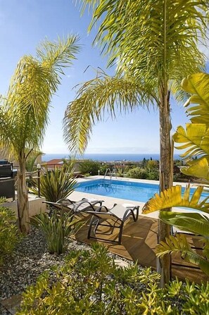 A pool area with lounge chairs, surrounded by tropical plants and a view of the ocean. - 3 Bed High Spec Villa in Tala /Amazing Sea Views/Heated Pool & Car Included (Tala)