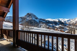 A wooden balcony with a view of snow-covered mountains and a village.