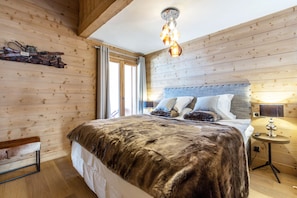 A wooden-paneled bedroom with a large bed, a wooden bench, and a hanging light fixture.