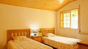 Une chambre avec deux lits simples, des têtes de lit en bois, une table de chevet avec une lampe et une fenêtre donnant sur un paysage verdoyant.