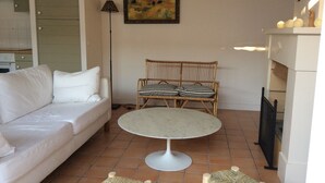 Un soggiorno con un divano bianco, una poltrona in vimini con cuscini a quadri, un tavolino rotondo e un quadro appeso al muro.