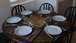Un tavolo da pranzo apparecchiato con piatti, bicchieri e posate, circondato da sedie, in una stanza con una finestra e un angolo cottura sullo sfondo.