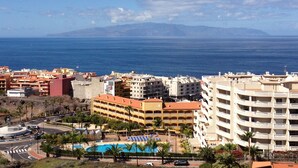 A coastal cityscape with a prominent hotel featuring multiple balconies and a swimming pool. - OFFER season 2025. Spectacular ocean and cliff views (Puerto Santiago. Los Gigantes)