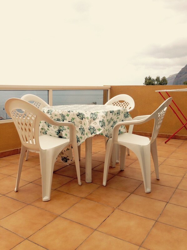 A terrace with a table and chairs, a view of the sea, and a mountain in the background.