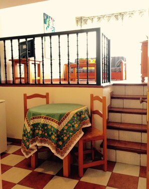 A dining area with a table covered by a patterned tablecloth, wooden chairs, and a staircase leading to an upper level.