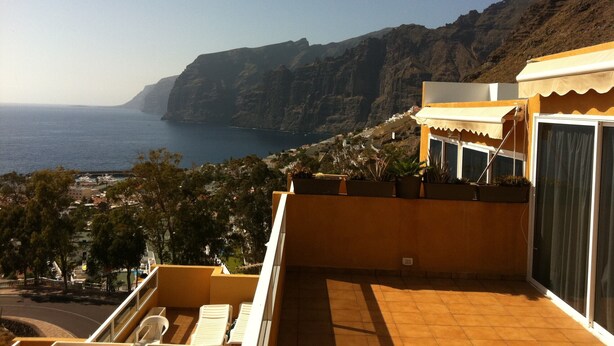 A coastal property with a terrace overlooking the sea, a mountain backdrop, and a view of a town below. - OFFER season 2025. Spectacular ocean and cliff views (Puerto Santiago. Los Gigantes)