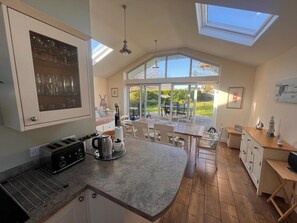 A modern kitchen with a large island, skylights, and a view of a garden. - Rhosneigr Beach Bungalow 2 Mins to Sea, Large Secure Garden, Open Fire, Sleeps 6 (Rhosneigr)