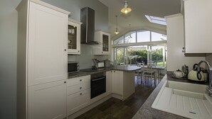 Une cuisine moderne avec des meubles blancs, un grand îlot central doté d’un évier et une vue sur l’extérieur grâce à de grandes fenêtres.