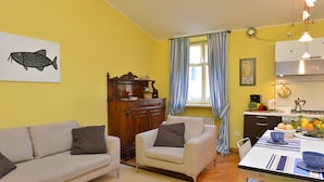 A living room with a sofa, armchair, and a dining table with a bowl and fruits.