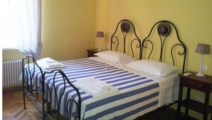 A single bed with a metal frame, a striped bedspread, two bedside lamps, and a window with curtains.