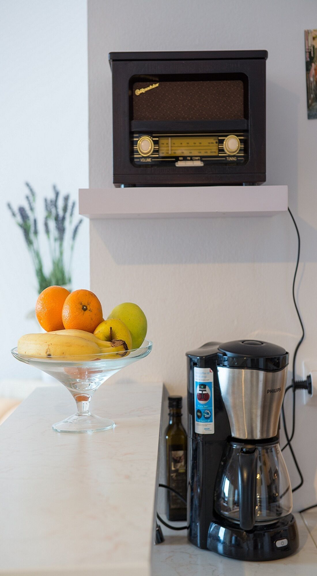 Un comptoir de cuisine avec une machine à café, un saladier en verre rempli de fruits et une radio ancienne.