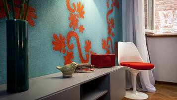 A modern room with a teal patterned wall, a white chair, a red cushion, a green vase, and a small bird figurine on a grey console table.