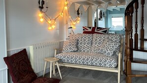 A cozy living room with a patterned sofa, a red armchair, and a small wooden stool. - Runswick Bay Top Gallant Cottage - outside seating  - sea and beach views (Runswick Bay)