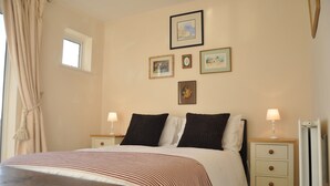 A bedroom with a bed, two bedside tables, a nightstand, a window, and wall-mounted pictures.