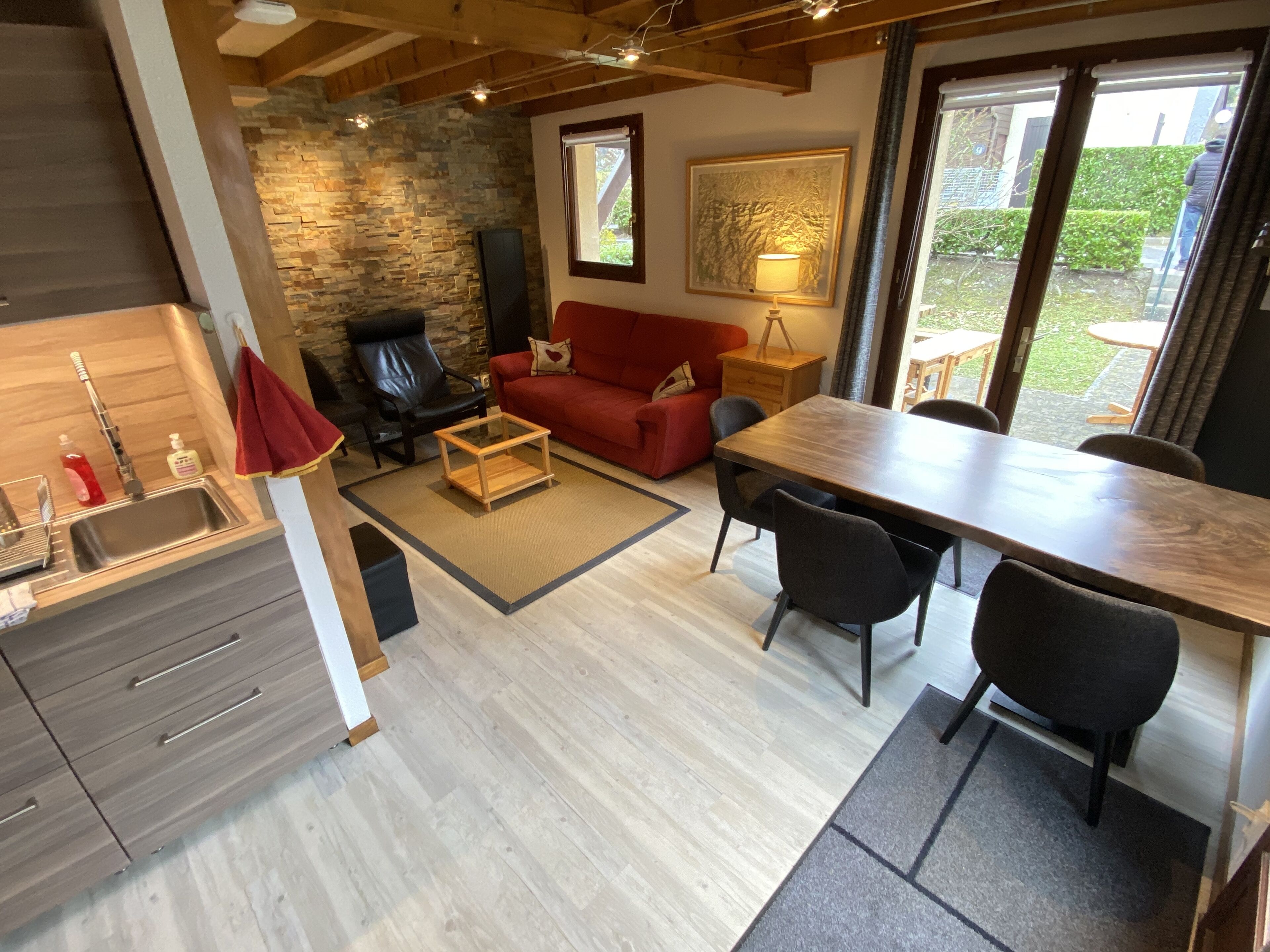 A modern kitchen with a stone wall, a red sofa, a wooden dining table, and a fireplace.