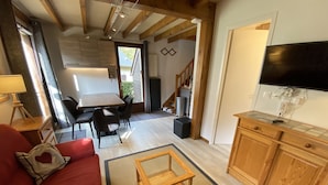 A cozy living room with a red sofa, a wooden coffee table, and a TV on a cabinet. There's a dining area with a table and chairs, and a kitchen in the background. - Chalet for 6 people in Cauterets with free parking space (Cauterets)