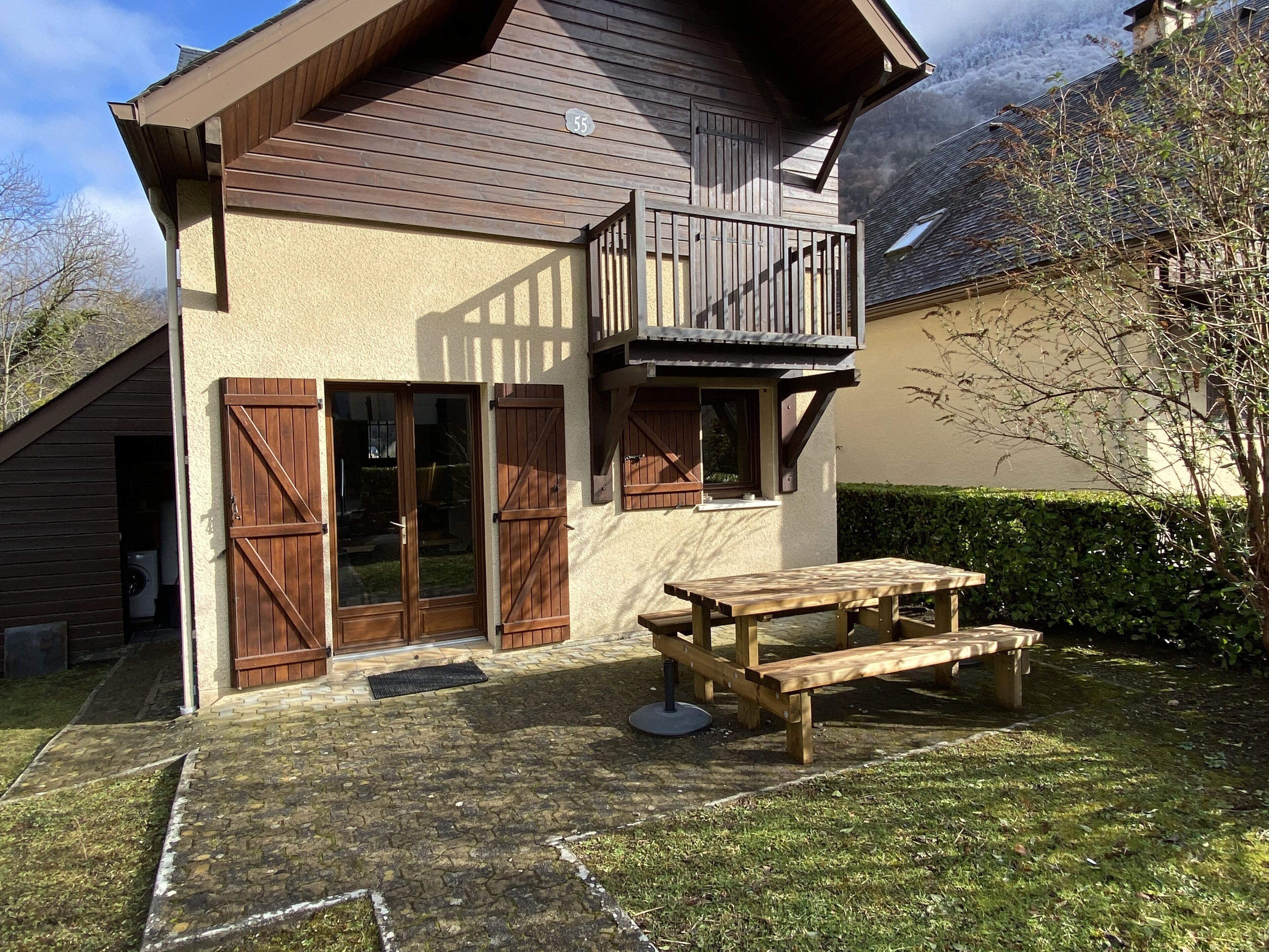Ein Haus mit einem Holzbalkon, einer Terrasse mit einem Holztisch und Bänken sowie der Hausnummer 55.