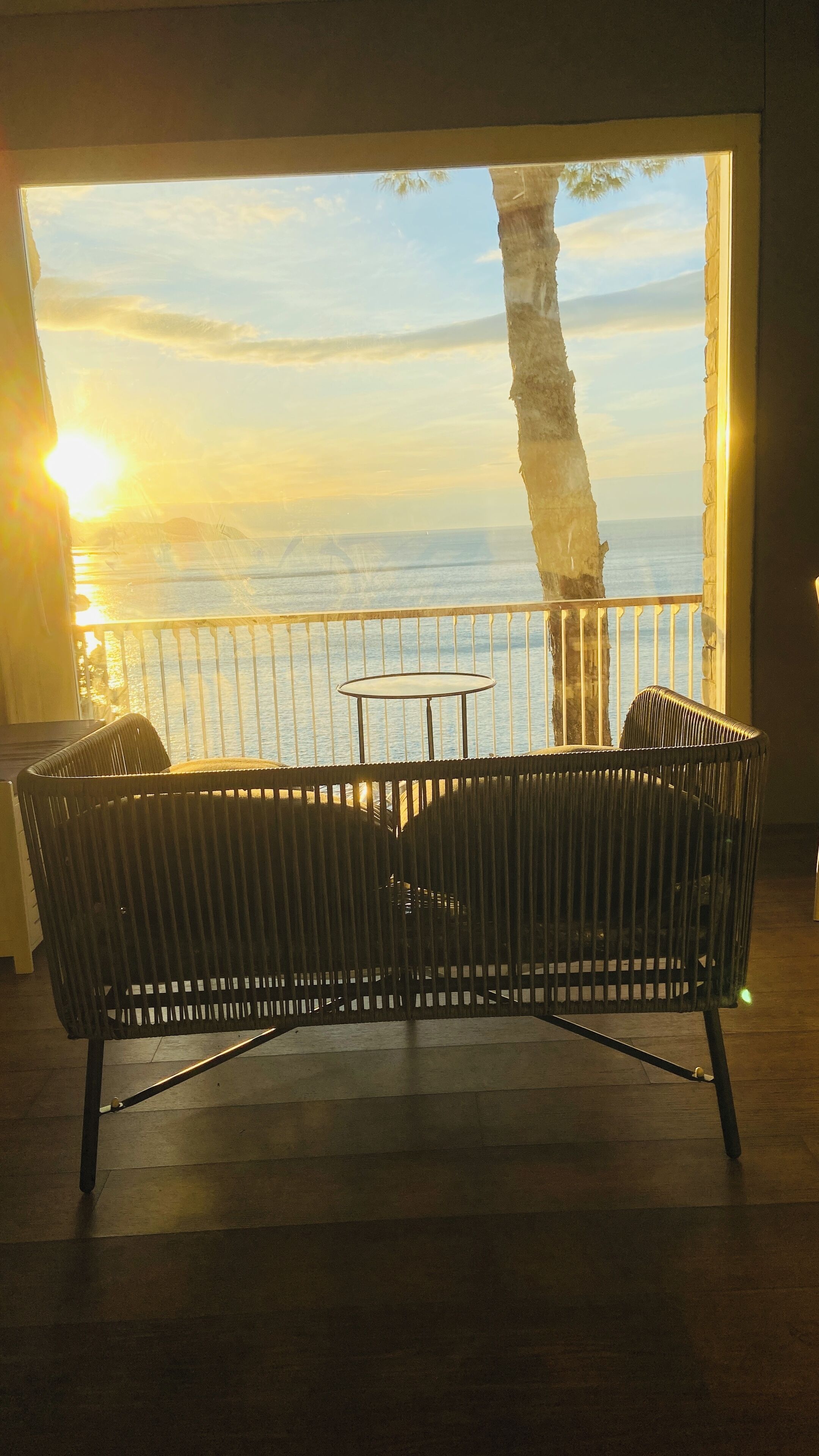 A balcony with a view of the sea at sunset, a table, and a chair.