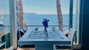 A dining area with a table and chairs, a vase with flowers, and a view of the sea through large windows.