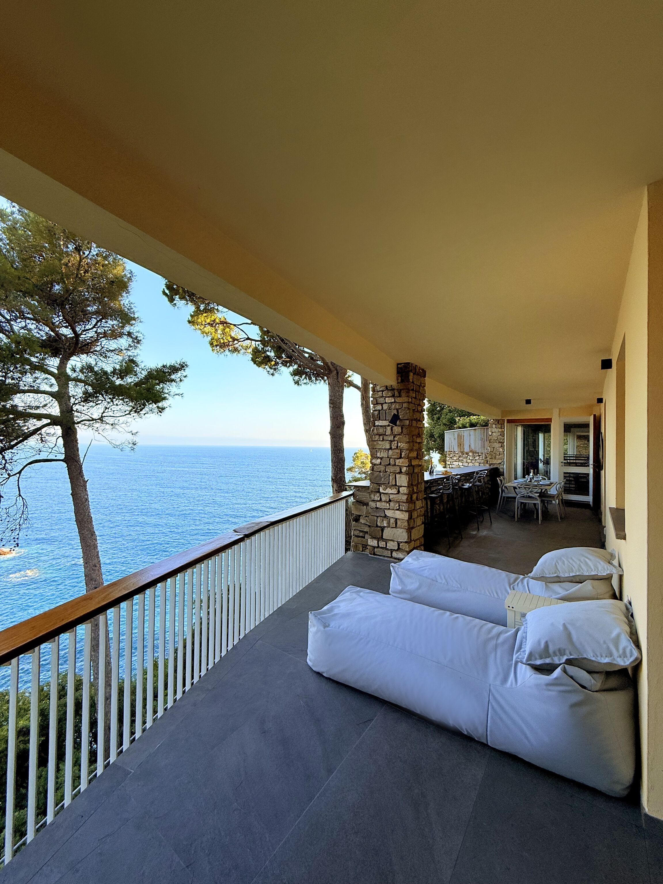 A balcony with a stone pillar, a sofa, and a view of the sea.