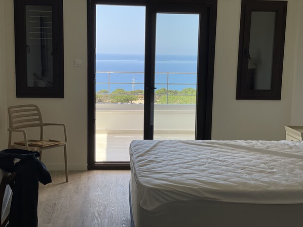 Une chambre à coucher avec un lit, une chaise, une fenêtre donnant sur la mer et une porte.