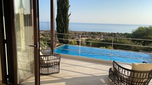 Un balcon avec une piscine, des fauteuils en osier et une vue sur la mer.