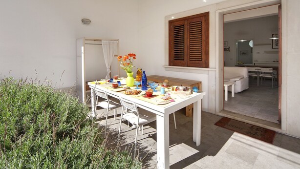 Un coin repas avec une table blanche dressée pour quatre personnes, entourée de verdure.
