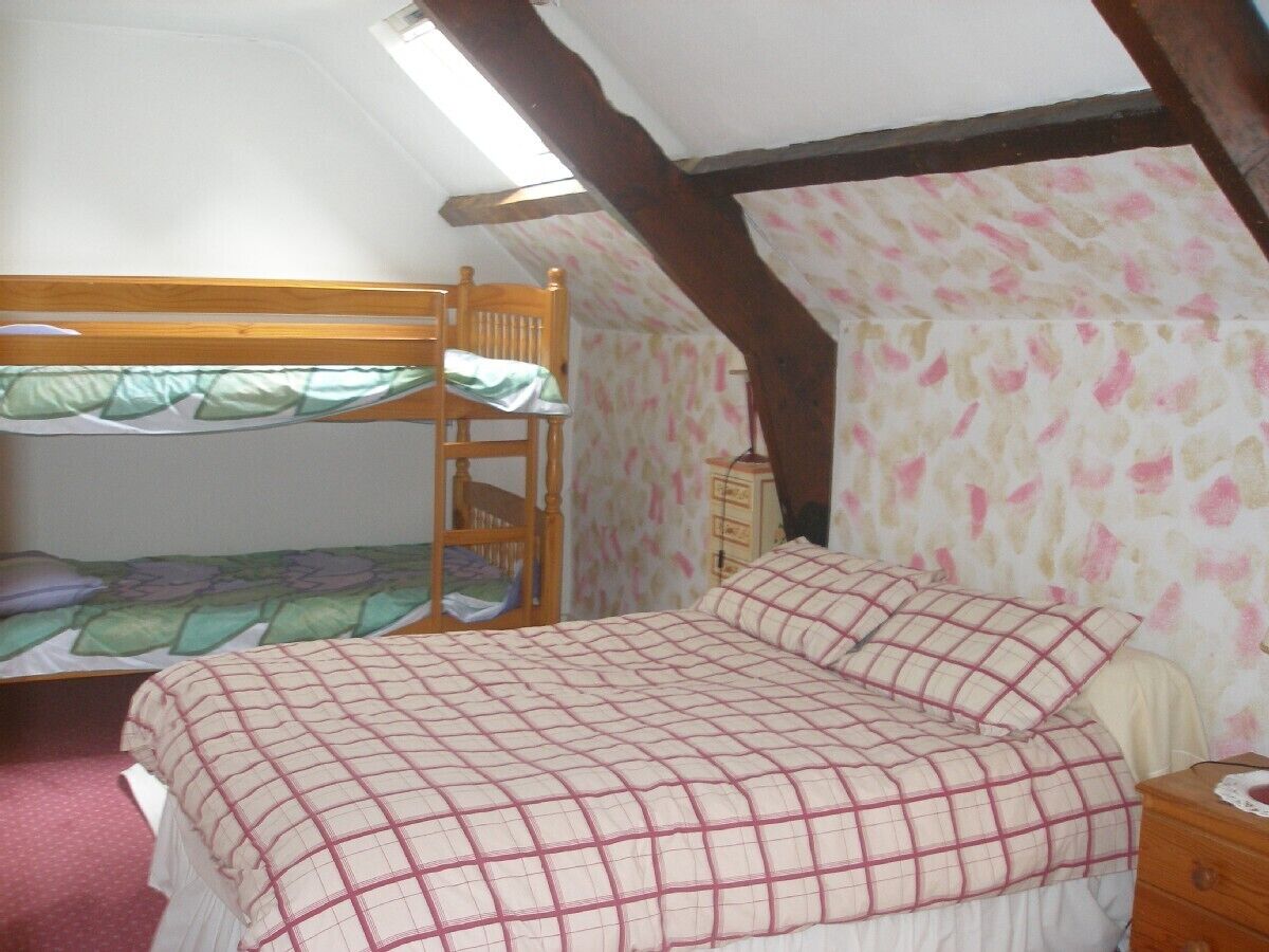 Een slaapzaal met een stapelbed, een enkel bed, een houten nachtkastje en behang met een patroon.