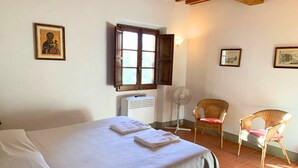 Un dormitorio con cama, dos sillas, una ventana y un aire acondicionado de pared.