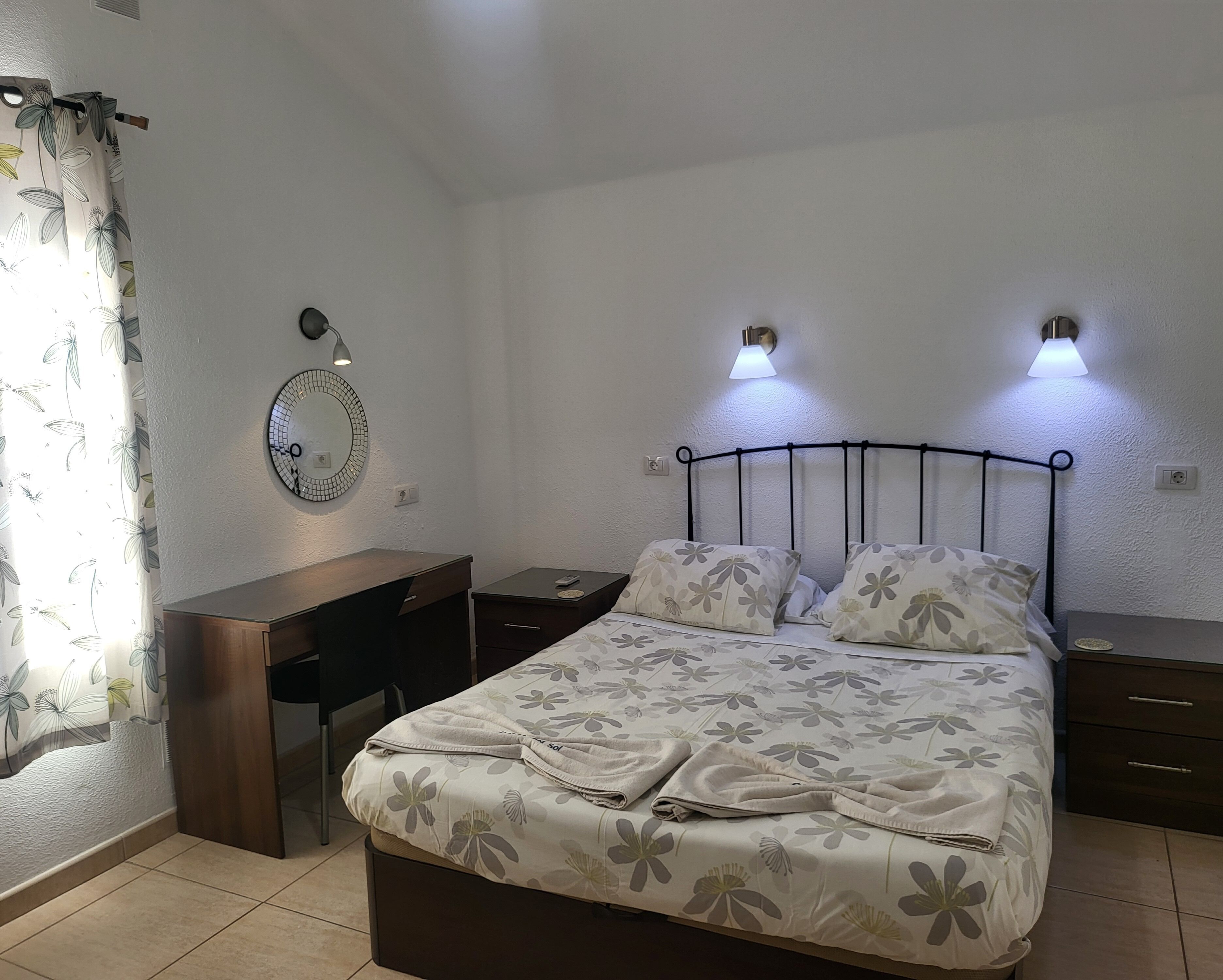 Een netjes ingerichte slaapkamer met een bed, nachtkastjes, een bureau, een spiegel en twee wandlampen.