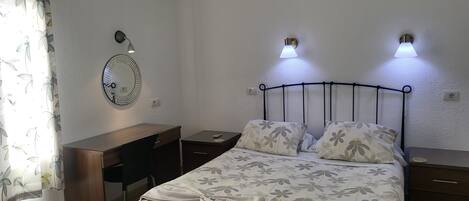 Een netjes ingerichte slaapkamer met een bed, nachtkastjes, een bureau, een spiegel en twee wandlampen.