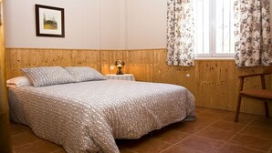 A bedroom with a wooden headboard, a bed with patterned bedding, a bedside table with a lamp, and a chair.
