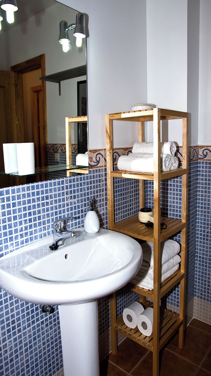A bathroom with a white sink, wooden shelves with towels, and a mirror with lights.