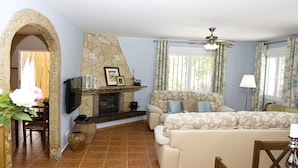 A living room with a stone fireplace, a sofa, a dining table with chairs, and a ceiling fan.