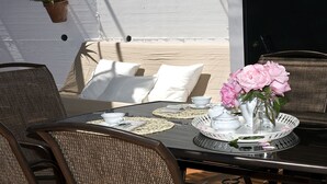 An outdoor dining area with wicker chairs, a table set with white dishes, and a vase of pink flowers.