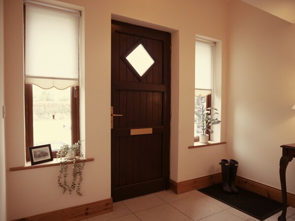 A wooden door with a diamond-shaped window, a potted plant on a shelf, and a pair of boots on a mat. - Beautiful Countryside With A Spectacular View Of The Mountains (Killarney)